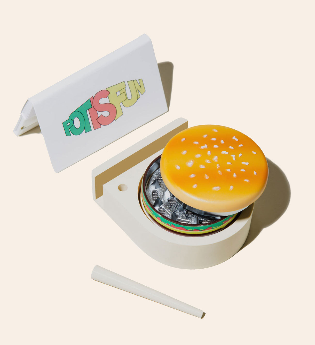 The tan Storage Solution with a Hamburger Grinder slightly opened, matching Joint Cone on the side, and with a pack of Pot Is Fun rolling papers on display